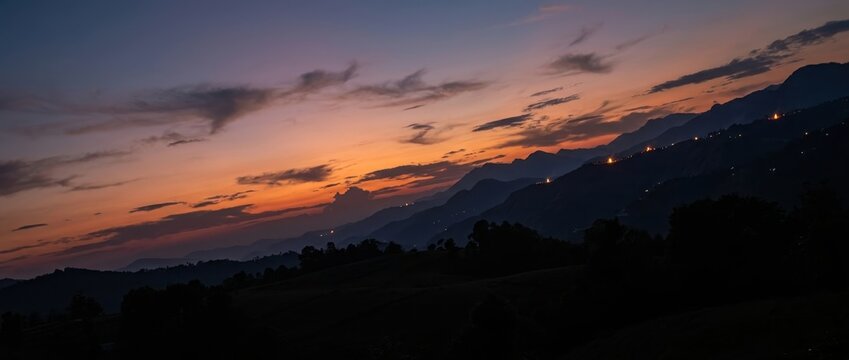 Mountain range silhouette at dusk with orange sunset sky and horizon lights
