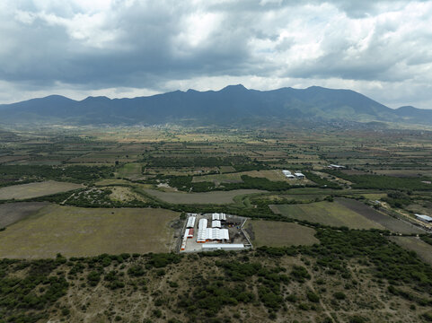 Aerial view of the Santiago Matatlan mezcal factory surrounded by rural agricultural fields and distant mountains under a cloudy sky in Santiago Matatlan, Oaxaca, Mexico.