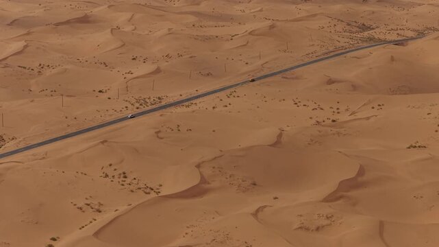 Aerial Top View of a Car Driving Along a Desert Road Surrounded by Golden Sand Dunes