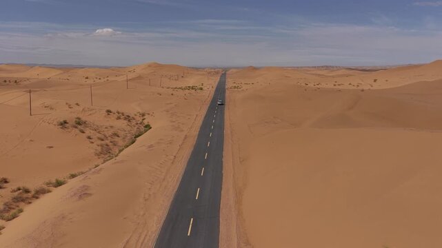 Aerial Top View of a Car Driving Along a Desert Road Surrounded by Golden Sand Dunes