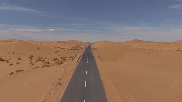 Aerial Top View of a Car Driving Along a Desert Road Surrounded by Golden Sand Dunes