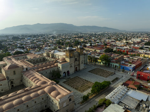 Aerial view of the historic Templo de Santo Domingo de Guzman with ornate facade and domes, overlooking colonial city rooftops and mountains in Oaxaca de Juarez, Oaxaca, Mexico.