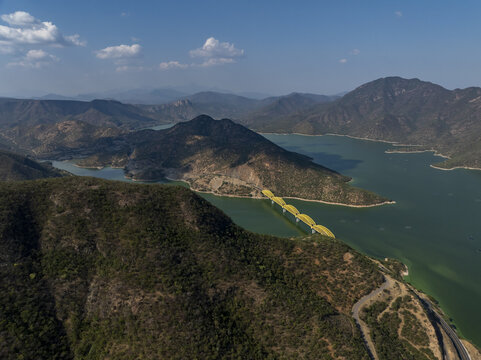 Aerial view of the yellow bridge spanning the Rio Balsas surrounded by rugged mountains and green water in Infiernillo, Michoacan, Mexico.