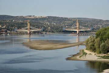 Obraz na płótnie Canvas Aerial view of low river water level on the Danube in Novi Sad, Serbia, with suspended cargo ship navigation and new bridge construction in the distance