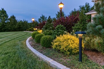 Obraz premium The Evening Garden Landscape With Curved Stone Border And Illuminated Lamps