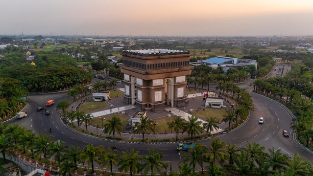 Aerial view of Simpang Lima Gumul Monument surrounded by palm trees and a circular road in Kediri, East Java, Indonesia.