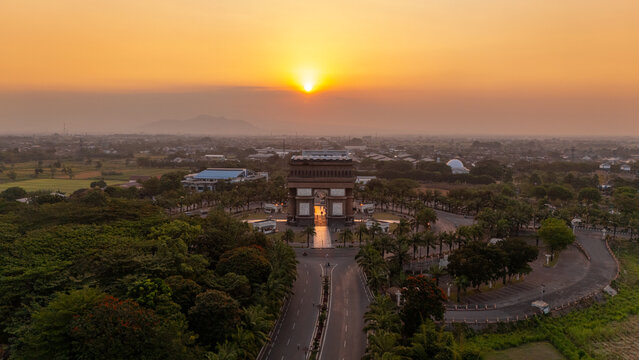 Aerial view of the Simpang Lima Gumul Monument surrounded by lush trees and roads during a golden sunset in Kediri, East Java, Indonesia.