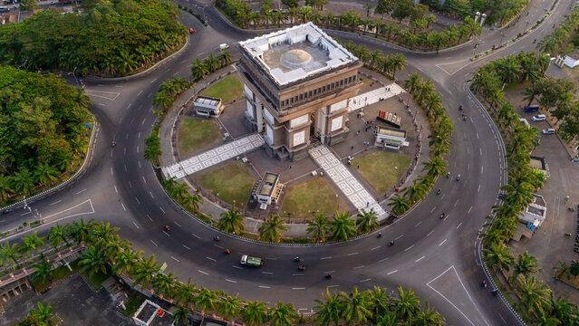 Aerial view of Simpang Lima Gumul monument surrounded by a circular road, lush palm trees, and manicured lawns in Kediri, East Java, Indonesia.
