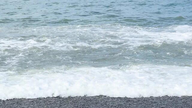 Blue sea and large waves and foam. Wave splashing over pebbles at sea. Rolling ocean waves. Summer beach background. Powerful sea waves	