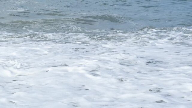 Blue sea and large waves and foam. Wave splashing over pebbles at sea. Rolling ocean waves. Summer beach background. Powerful sea waves	