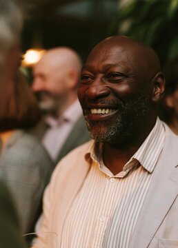 Close-up portrait of a middle-aged african-american man with a big smile on his face. he is wearing a light pink striped shirt and a beige blazer.