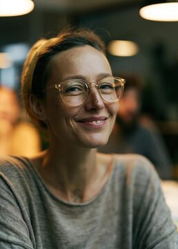 Close-up portrait of a young woman with a big smile on her face. she is wearing a gray t-shirt and gold-framed glasses.