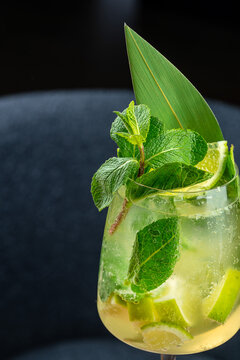 Refreshing cocktail with mint leaves, lime slices, and a decorative green leaf in a clear glass on a dark background