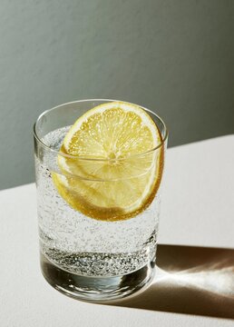 Glass of water with a slice of lemon on top. the glass is filled with clear water and there are small bubbles visible on the surface.
