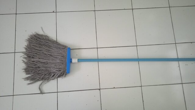 Traditional Floor Mop with Blue Handle Resting on White Ceramic Tile Floor