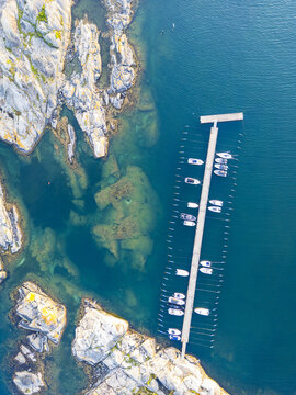 Aerial view of a wooden pier with moored boats in the clear blue waters of the rocky coastline in Lerkil, Halland County, Sweden.