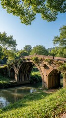 Fototapeta premium Old stone arch bridge spans calm river water. Lush green trees, foliage surround ancient structure. Peaceful parkland offers tranquil nature scene.