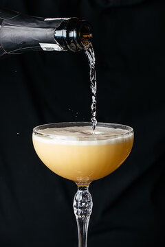Champagne being poured into a crystal coupe glass with a frothy surface against a black background, highlighting the drink's golden hue and effervescence