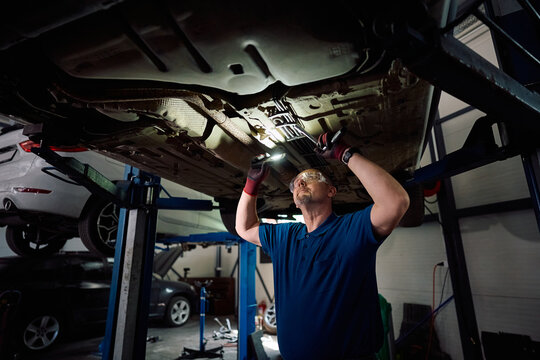Auto mechanic inspecting vehicle chassis in repair shop.