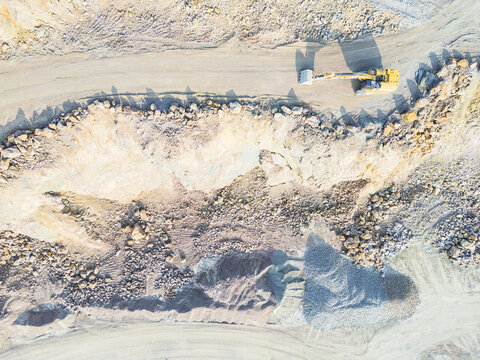 Aerial view of an excavator working in a stone quarry on Hisingen, with piles of gravel, rocky terrain, and dusty ground in Gothenburg, Vastra Gotaland Count, Sweden.