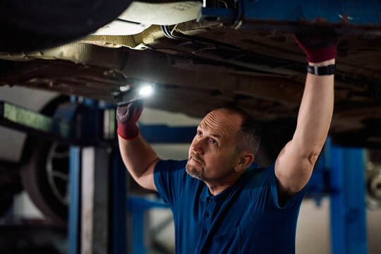 Mature mechanic checking condition of car undercarriage in garage.