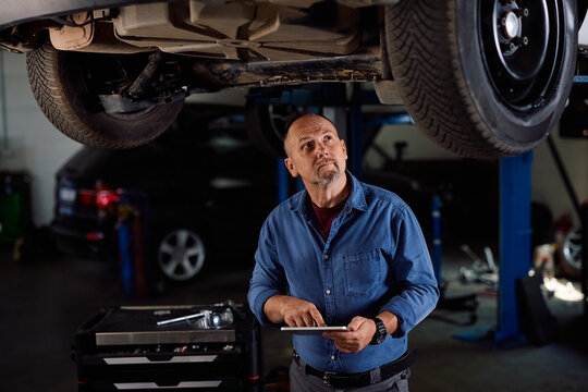 Car service worker using touchpad while inspecting chassis and suspension system of vehicle.