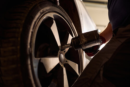 Close up of technician using pneumatic wrench while changing tire on vehicle.