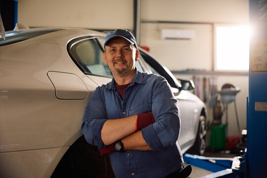 Happy car mechanic with arms crossed in garage looking at camera.