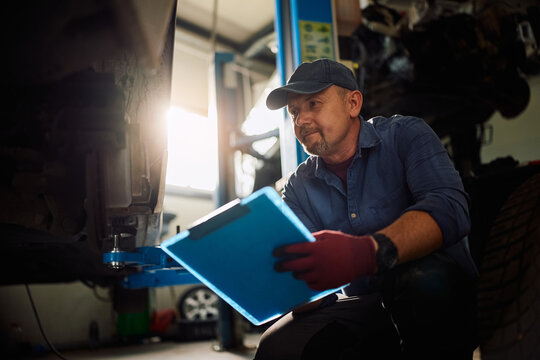 Mature mechanic taking notes during vehicle inspection in workshop.