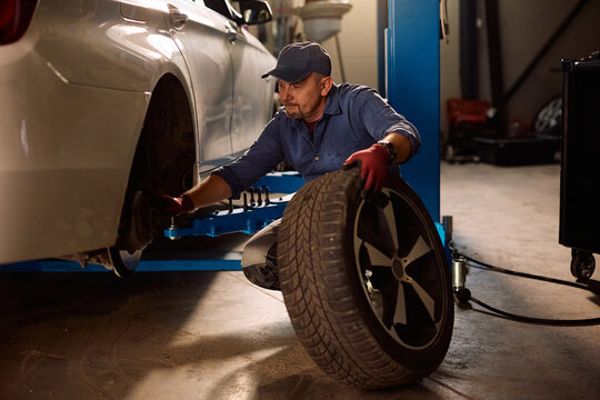 Mature mechanic replacing tire during car maintenance in garage.