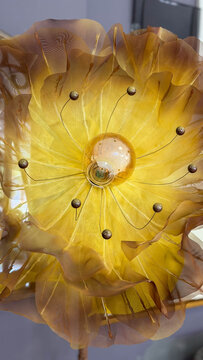 Close-up of decorative flower-shaped lamp with translucent golden fabric petals and glowing light bulb, creative floral lighting design.