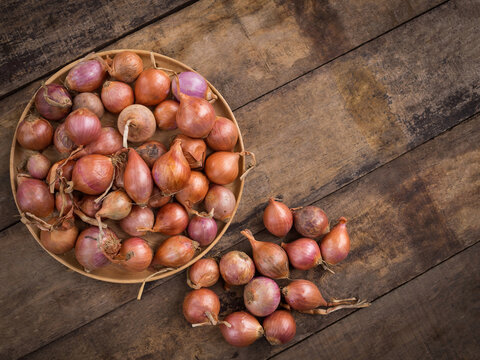 Fresh raw shallots in wooden plate on rustic dark wooden table with copy space.