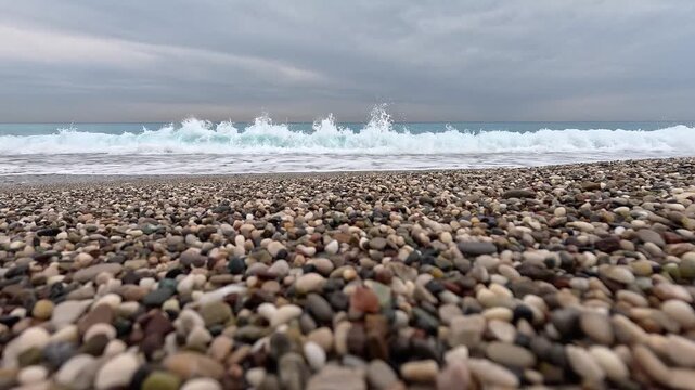 Ocean waves crashing on smooth pebble beach under overcast sky in cinematic slow motion video clip.