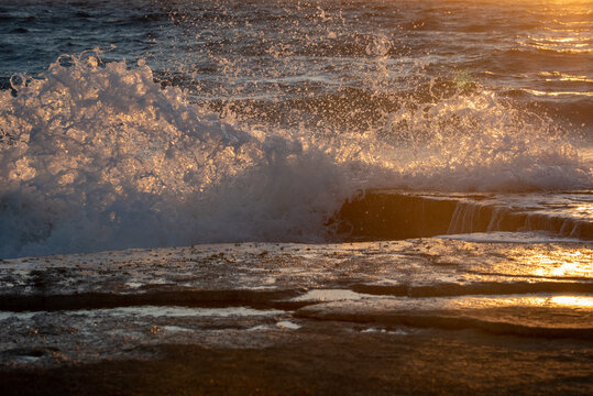 Stormy windy sea waves splashing on a rocky seashore at sunset