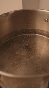 Water heating and beginning to boil in a stainless steel pot on a gas stove, with visible steam and bubbles during the cooking process.
