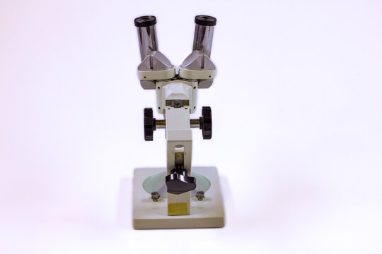 Back view of an old laboratory microscope isolated on white, showing the metal body, adjustment knobs, eyepieces and electrical cable.