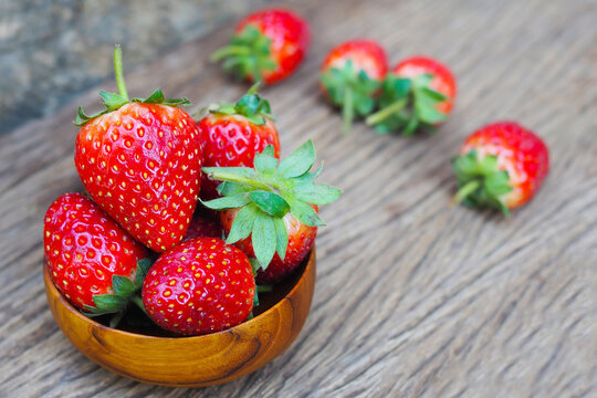 Fresh ripe red strawberries in a wooden bowl on a rustic wooden background.