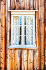 White framed window with lace curtains on weathered wooden wall © Lars Johansson