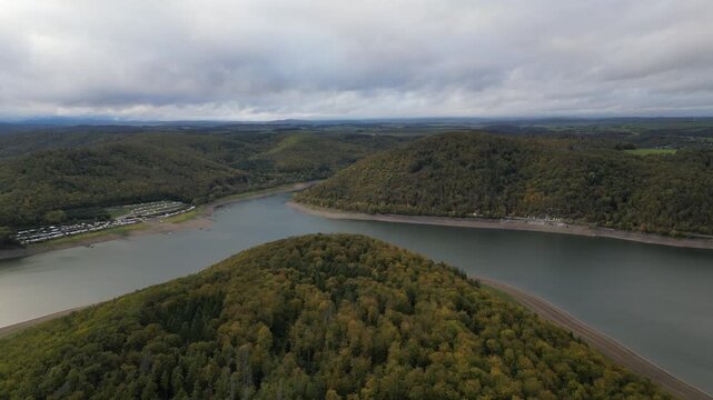 Scenic aerial view of the forested hills around Eschelberg mountain and a tranquil reservoir in Hesse, Germany. Captures the lush natural beauty and a peaceful campground area.