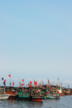 Fishing boats with red flags docked in the harbor under clear sky
