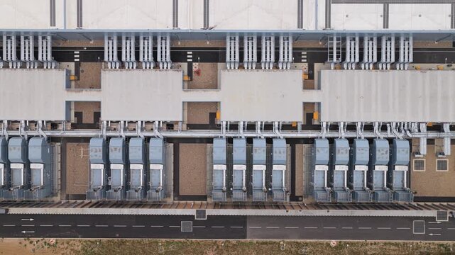 Rows of cooling systems operate on the roof of a large industrial data center complex during a clear day with paved roads visible around the perimeter of the infrastructure building