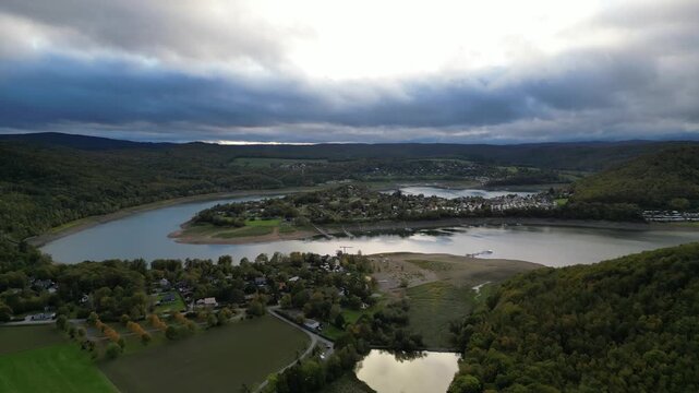 Aerial drone footage showing the Edersee reservoir and Scheid village in Hesse, Germany. The Eder river flows into this scenic lake with low water levels, surrounded by lush green hills.