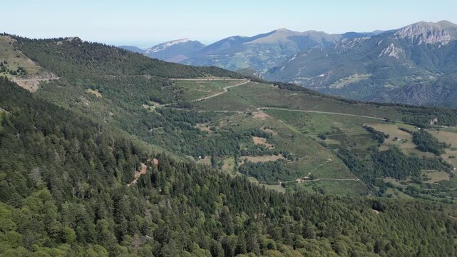 Stunning aerial perspective of winding roads carving through the forested slopes and lush valleys of Col d'Aspin in the Pyrenees mountains in Occitania, France, under a clear blue sky.