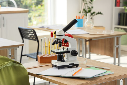 Microscope and test tubes on a wooden desk in a bright science classroom, education and scientific research