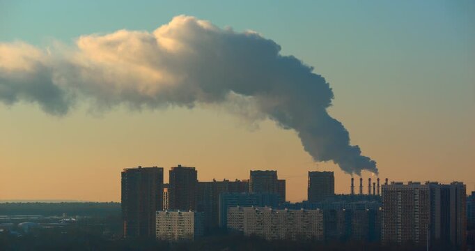 Massive industrial emission plume streams from multiple chimneys and spreads above dense apartment towers in golden sunset light creating a stark urban air pollution and environment scene at dusk
