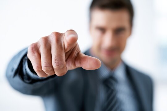 Businessman in suit pointing directly at the camera with blurred face in office setting conveying assertiveness and engagement
