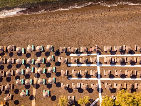 Top down drone view of straw sun umbrellas and sunbeds on black sand beach in Perissa Santorini Greece