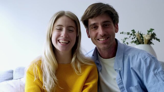 A cheerful young couple enjoys a lively video call or records a vlog from their home. They share smiles, laughter, and engaging conversation, radiating happiness and connection in a modern, casual set