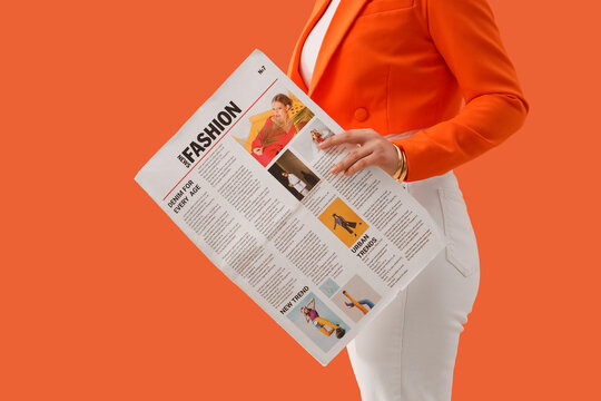 Woman in orange blazer and white pants holding a fashion newspaper with articles on urban trends and new styles, the publication features various images and text, current fashion information and media