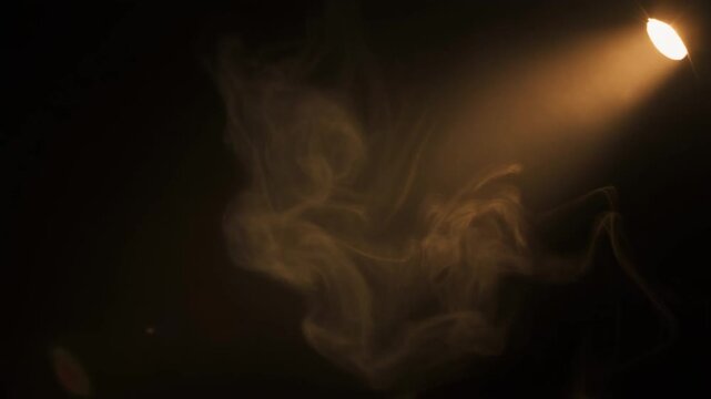 Warm light beam sweeps through thin drifting smoke, selectively illuminating passing tendrils against total darkness while clean negative space remains on left, creating dramatic cinematic contrast
